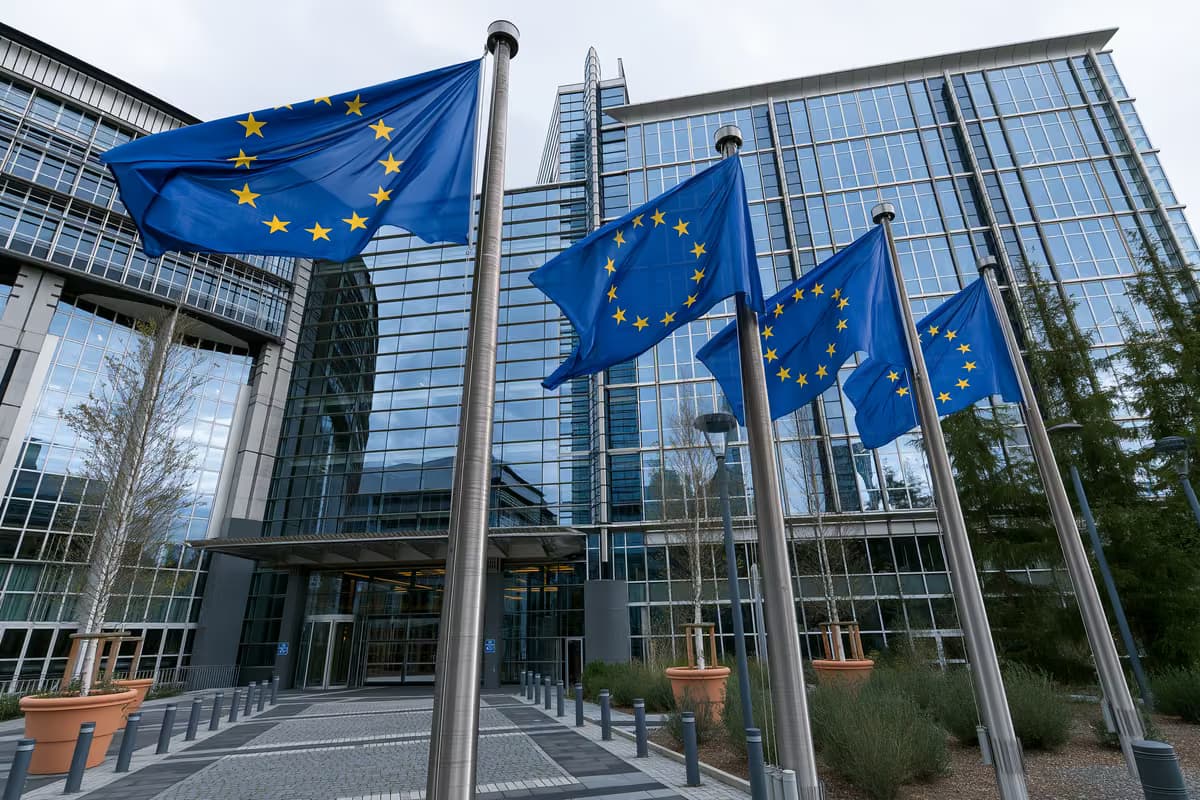 Európai uniós zászlók zászlórudakon egy modern üvegépület előtt.