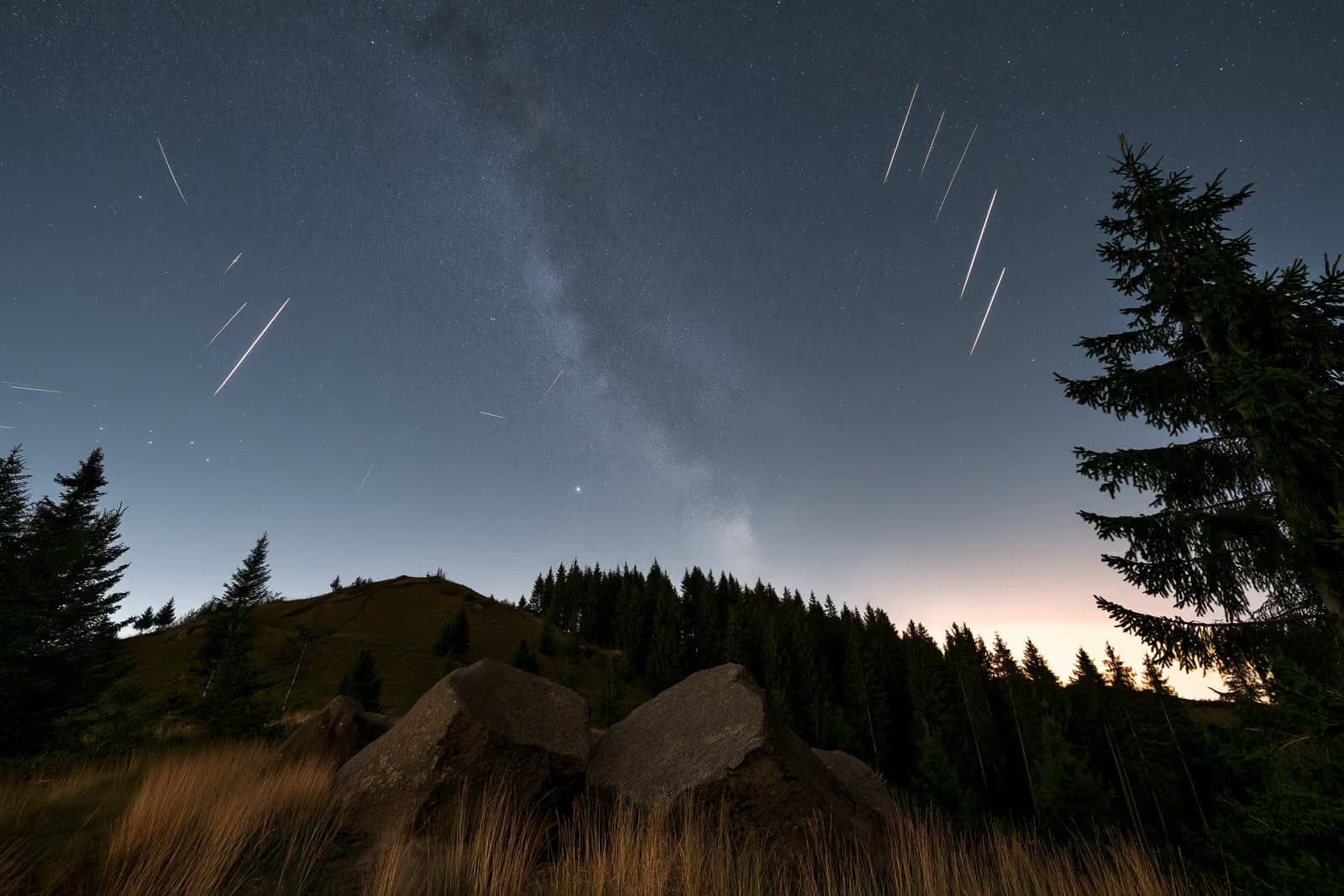 Éjszakai égbolt egy sötét német vidék felett, meteorcsíkokkal és halvány csillagsávval a fejük felett.